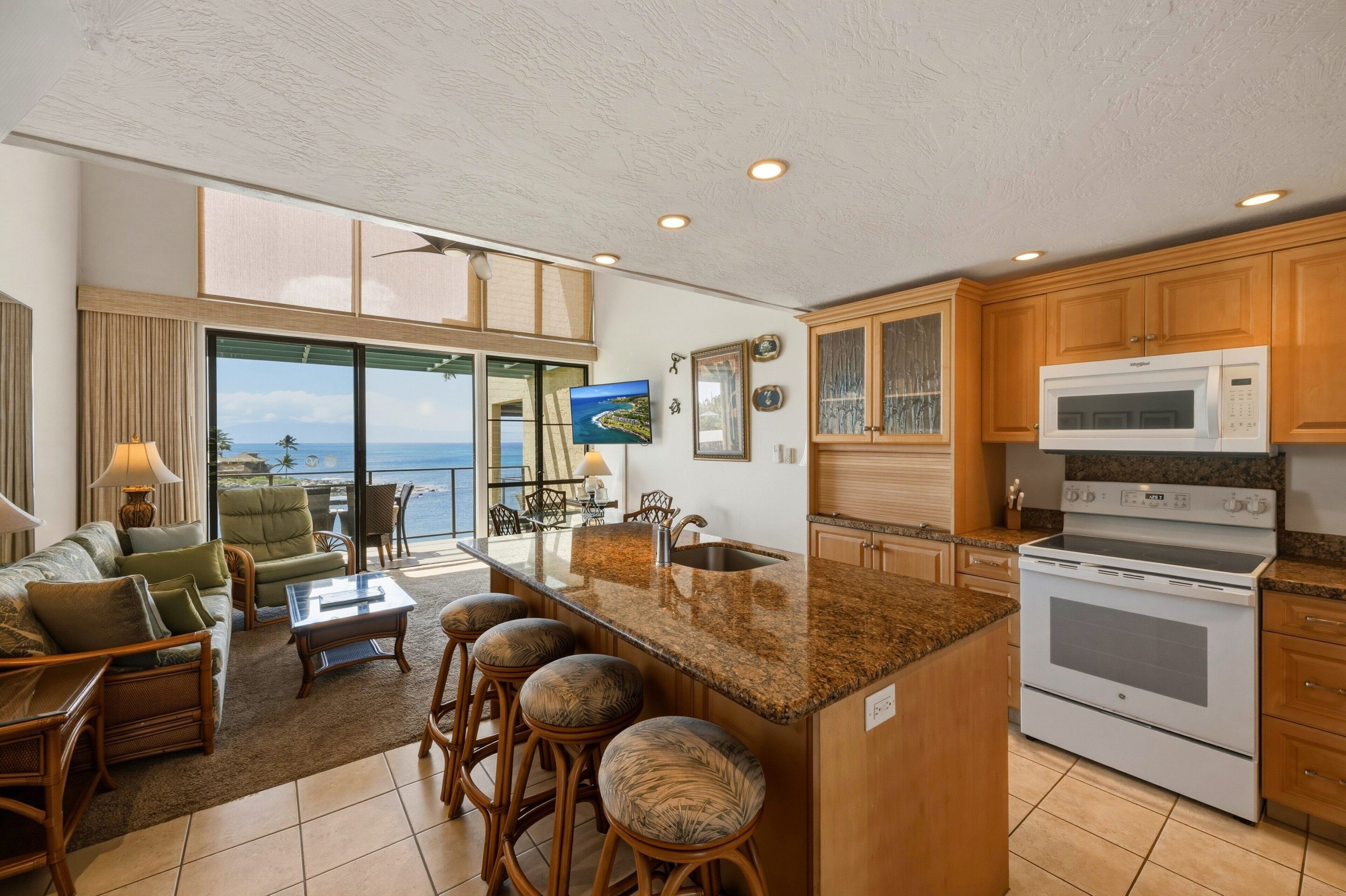 A kitchen with a large island, a microwave, and a stove. There is a dining area with a view of the ocean.