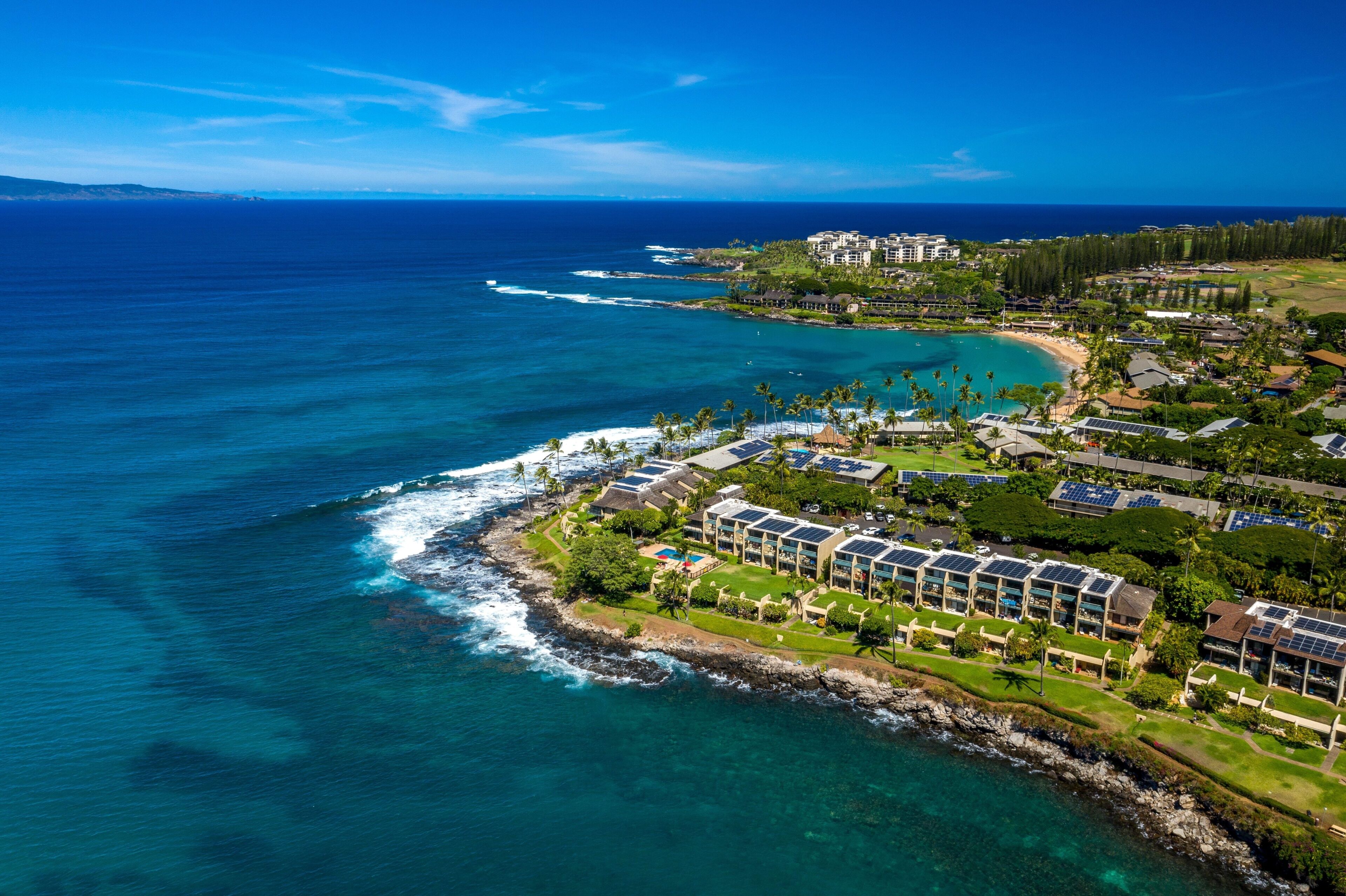 An aerial view of a coastal resort with multiple buildings, a beach, and a rocky shoreline.