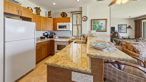 A kitchen with wooden cabinets, a white refrigerator, a microwave, an oven, a sink, and a ceiling fan. - Oceanfront Maui Retreat At Napili Point - Unit B16 1 Bedroom Condo (Lahaina)