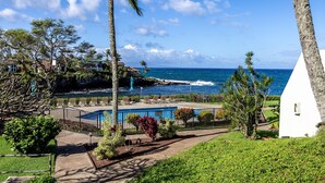 A pool area with lounge chairs, a small white building, and a view of the ocean. - Oceanfront Maui Retreat At Napili Point - Unit B16 1 Bedroom Condo (Lahaina)