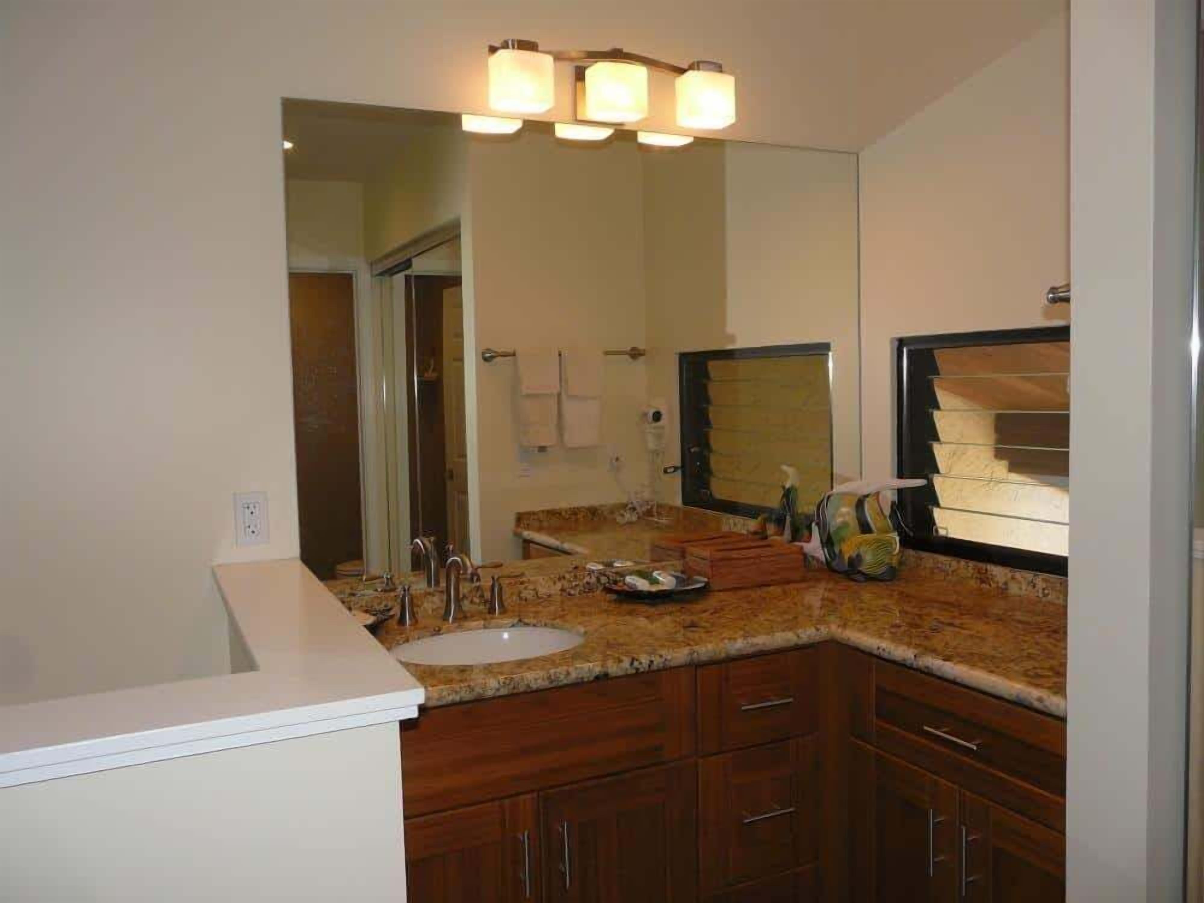 A bathroom with a sink, mirror, vanity, and a shower area.