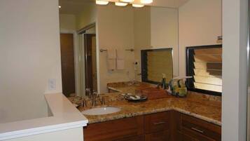 A bathroom with a sink, mirror, vanity, and a shower area.