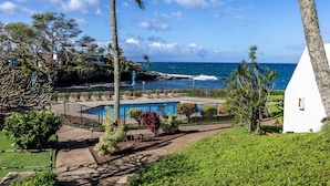 Ein Poolbereich mit Liegestühlen, ein weißes Gebäude und Blick aufs Meer.