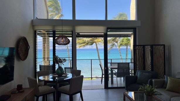 A spacious living area with a large window overlooking the ocean, a ceiling fan, and a dining area with chairs and a table. - Napili Point Point Oceanfront 2br Loft - Unit C2 1 Bedroom Condo (Lahaina)