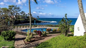 A pool area with lounge chairs, a white building, and a view of the ocean. - Oceanfront Condo Near Napili Bay 1br - Unit B19 1 Bedroom Condo (Lahaina)