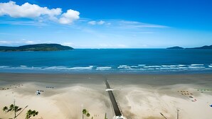 A beach with a long road leading to the water, surrounded by sand and sparse vegetation. - Clube XV (Santos)