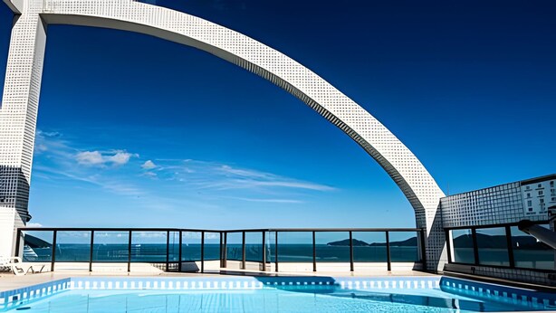 A swimming pool with a clear view of the ocean and a distinctive white arch structure. - Clube XV (Santos)