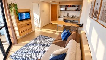 A modern living room with a sofa, a television, and a kitchen area with shelves.