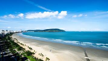 Paisagem costeira urbana com uma praia extensa, uma pequena ilha e um céu azul límpido.