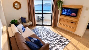 A living room with a sofa, TV, and a view of the sea.