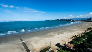 A wide beach with a clear sky, calm sea, and distant mountains. - Clube XV (Santos)