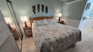 Un dormitorio con una cama, dos mesitas de noche con lámparas, un espejo y una pared decorada.