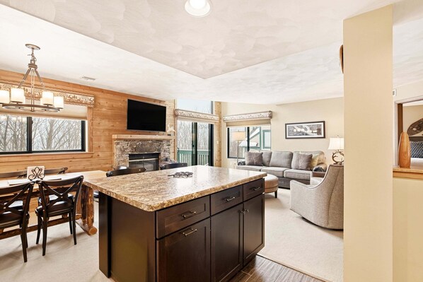 A modern kitchen with a large island, wooden cabinetry, and a stone fireplace. - Seven Springs Meadowridge 3brloft Premier-cssv8011 3 Bedroom Condo (Champion)