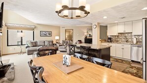 A modern kitchen with stainless steel appliances, a dining area with a wooden table and chairs, and a living room with a sofa and chairs. - Seven Springs Meadowridge 3brloft Premier-cssv8011 3 Bedroom Condo (Champion)