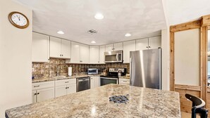 A kitchen with white cabinets, a granite countertop, a stainless steel refrigerator, a microwave, and a clock on the wall. - Seven Springs Meadowridge 3brloft Premier-cssv8011 3 Bedroom Condo (Champion)
