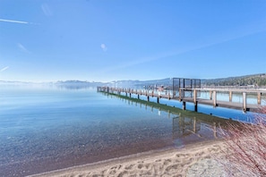 A clear lake with a wooden pier extending into the water, surrounded by calm water and distant mountains. - Tahoe City - Lake Forest Condo 3 Bedroom Condo (Tahoe City)
