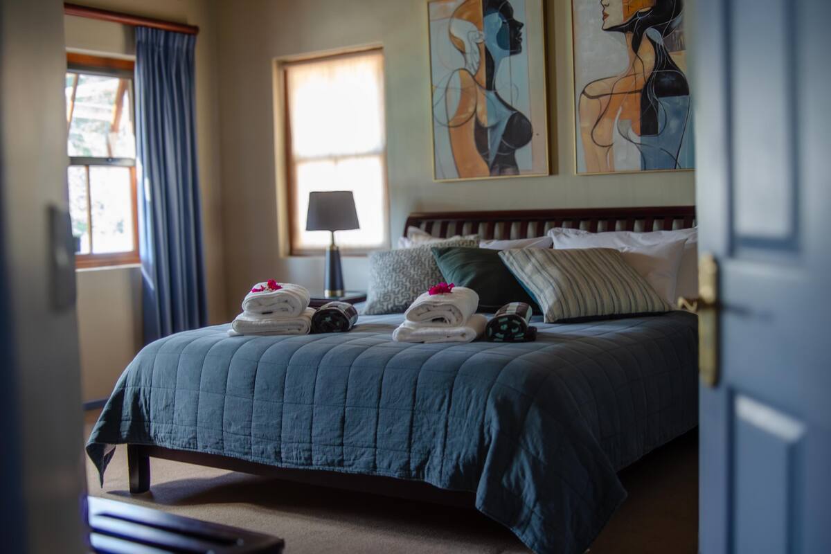 A neatly made bed with pillows and folded towels, a bedside lamp, and artwork on the wall.