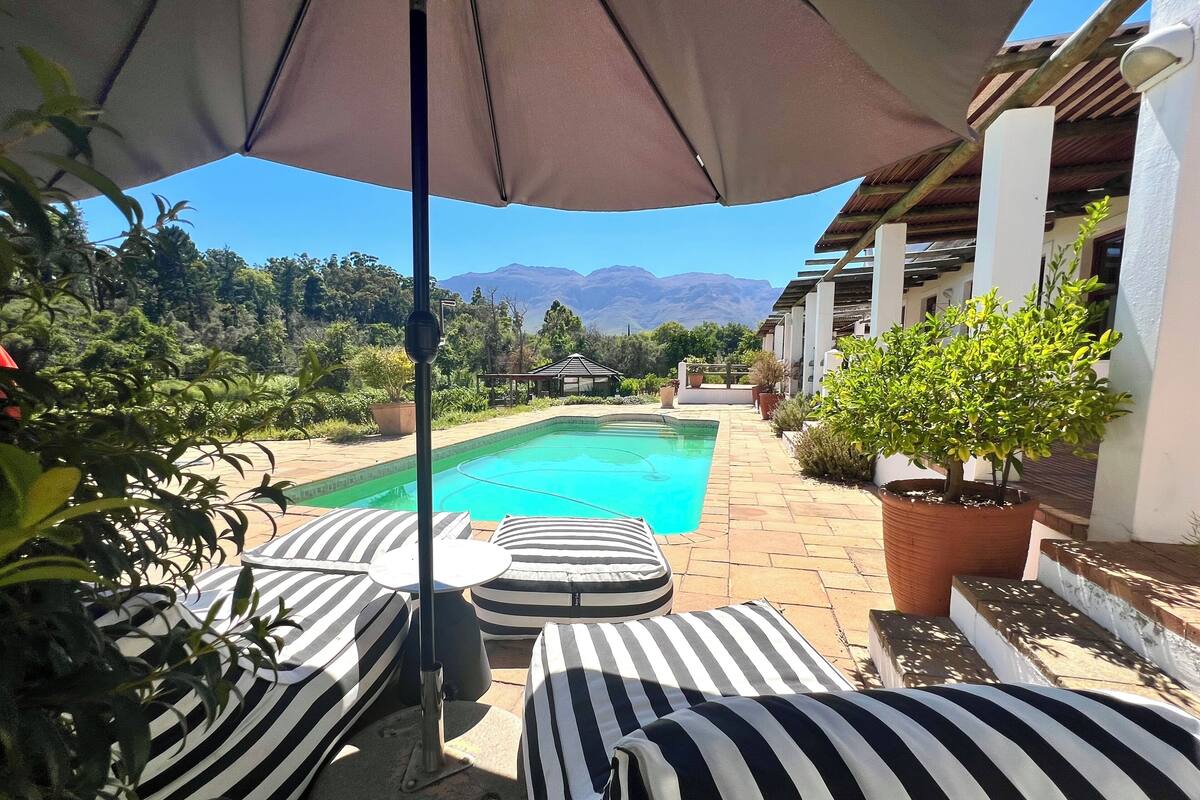 A pool area with striped lounge chairs and a pergola overhead.