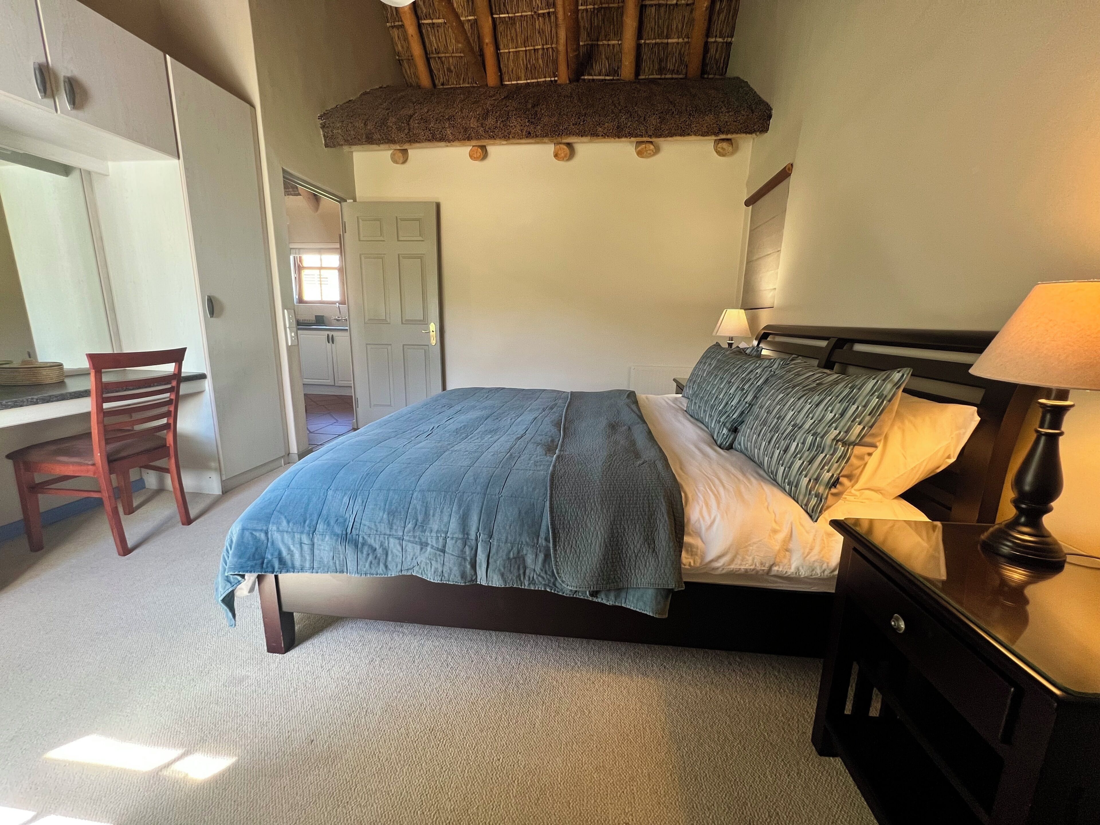 Een slaapkamer met een bed, nachtkastje, lamp, stoel en een deur naar een badkamer.