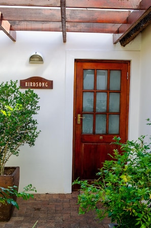 Una puerta de madera con un panel de vidrio, un letrero que dice 'BIRDSONG' y una planta en maceta a la izquierda.