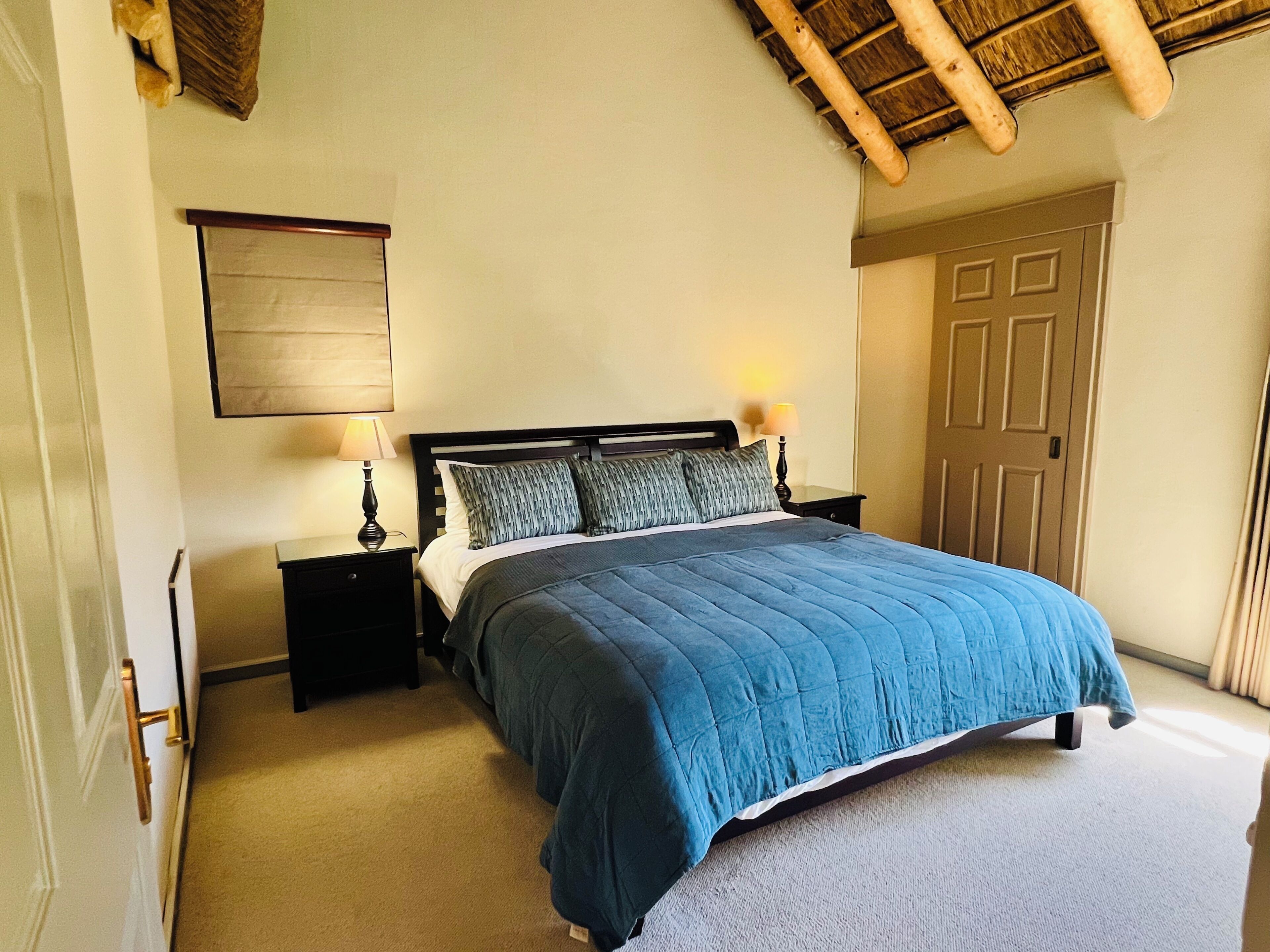 Une chambre à coucher comprenant un lit, deux tables de chevet, une commode, une porte et un plafond avec des poutres apparentes.
