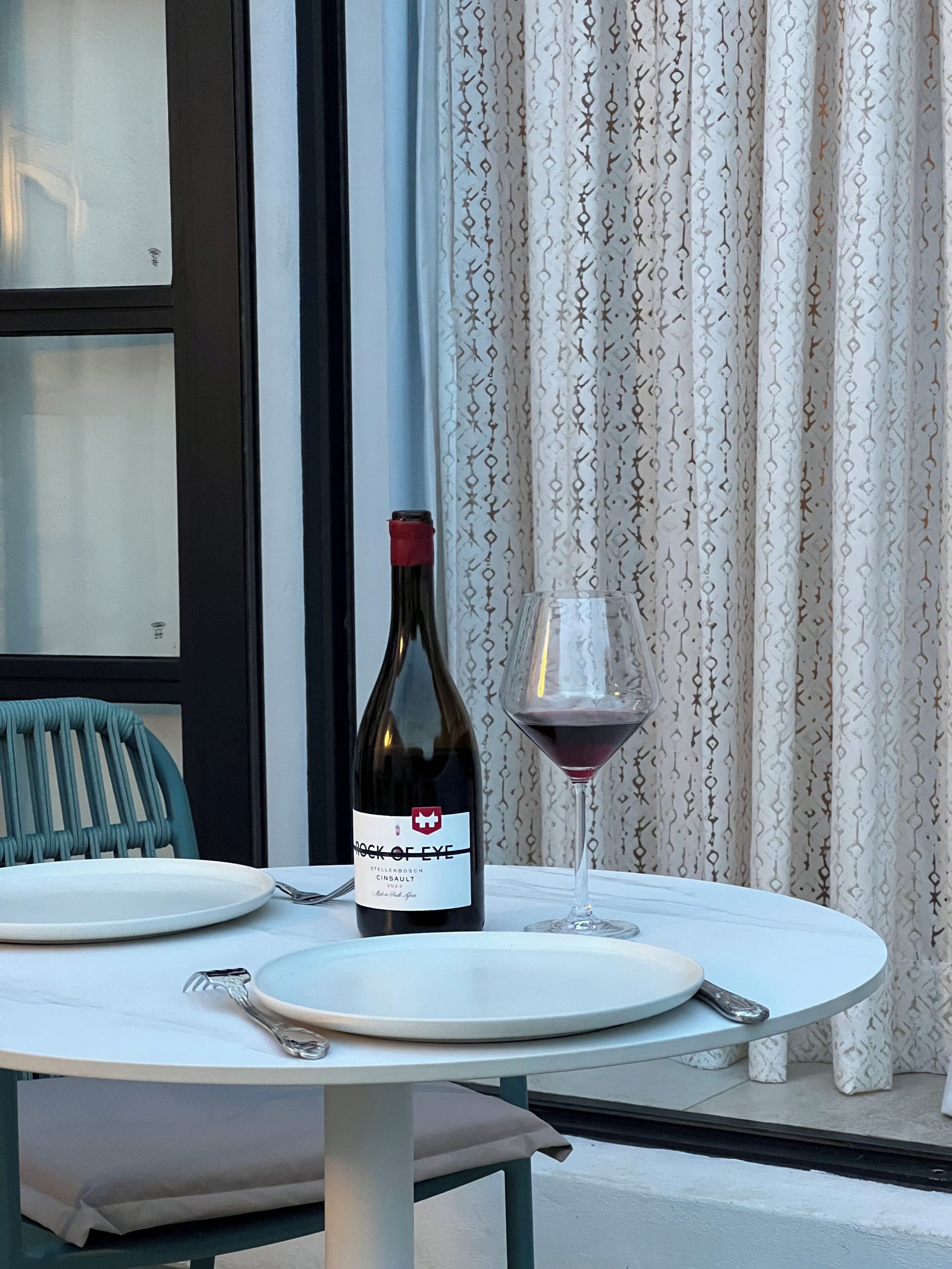 A dining table with a wine bottle and glass, a chair, and a window with curtains.