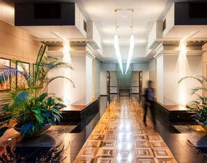 A hotel lobby with a long corridor, potted plants, and a modern light fixture. - Spacious Melbourne CBD Apartment | Sleeps 6 | Family Friendly | Parking Included (Melbourne)
