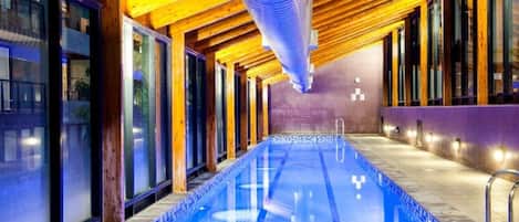 Une piscine intérieure avec des poutres en bois et des murs en verre.