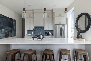 Une cuisine moderne avec des meubles blancs, un réfrigérateur en acier inoxydable et un grand îlot central doté de tabourets de bar.