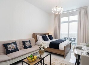 A hotel room with a bed, sofa, dining table, and a view of the city. - Vogue | Skyz by Danube near Dubai Miracle Garden (Dubai)