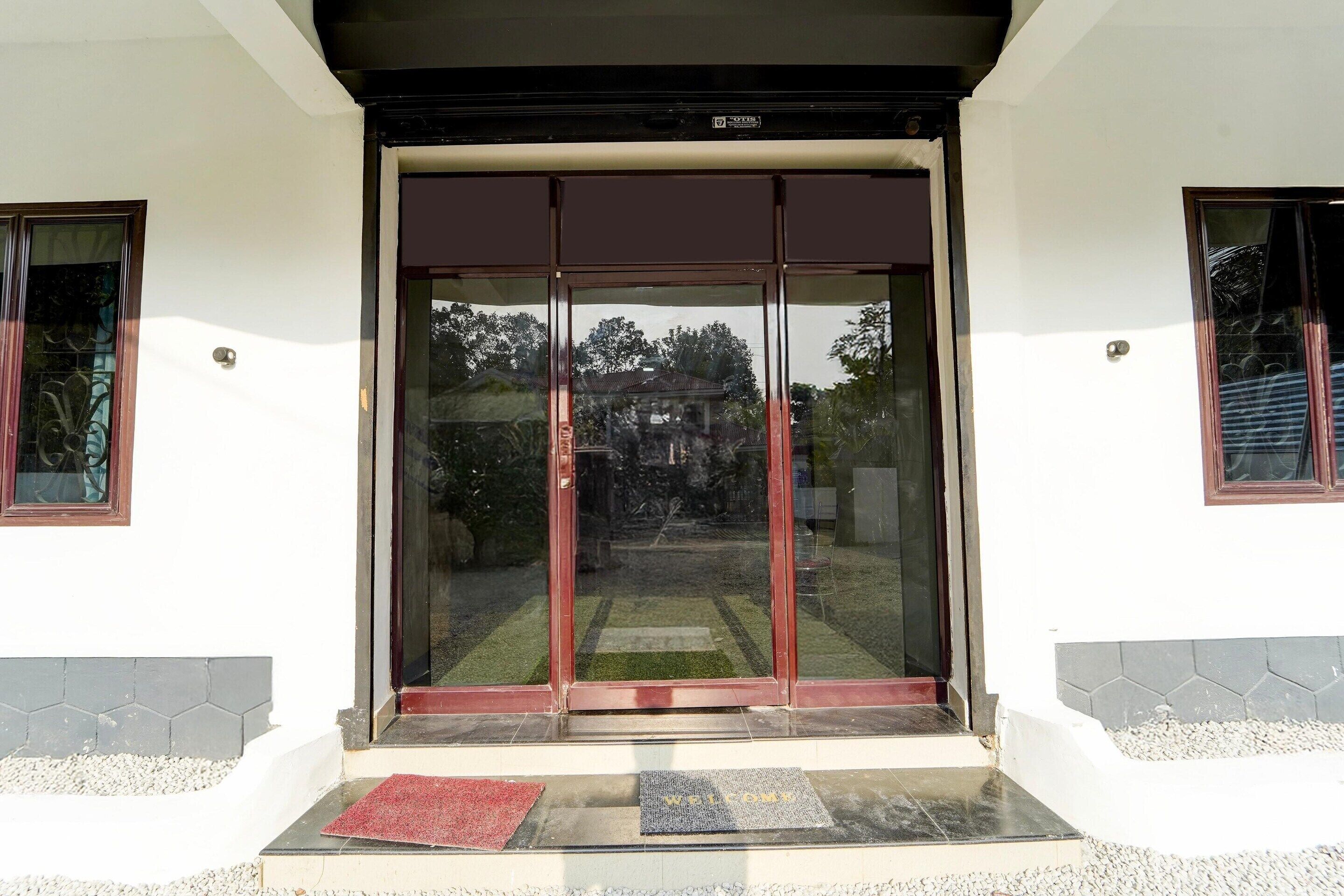 A building entrance with a sliding glass door, a red mat, and a welcome mat.