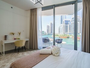 A modern hotel room with a large bed, a desk, and a view of a cityscape and water. - Lavish 2BR with Balcony-Full Marina View (Dubai)