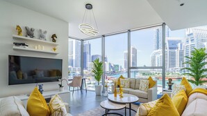 Una sala de estar moderna con un televisor grande, asientos cómodos, una mesa de centro y vistas a un horizonte urbano.