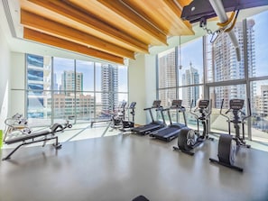 A gym with treadmills, stationary bikes, and weight machines, large windows with a city view. - Lavish 2BR with Balcony-Full Marina View (Dubai)