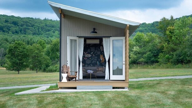 A small cabin with an open door, a chair, and a table outside. - Tiny House 4 - Farm Sanctuary, Finger Lakes (Watkins Glen)