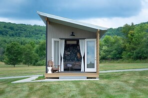 A small cabin with an open door, a chair, and a table outside. - Tiny House 4 - Farm Sanctuary, Finger Lakes (Watkins Glen)