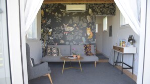 A cozy living room with a grey sofa, a small round table, and a floral-patterned wall. - Tiny House 4 - Farm Sanctuary, Finger Lakes (Watkins Glen)