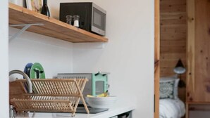 A kitchen with a white countertop, grey cabinets, a wooden shelf, and a microwave. - Tiny House 4 - Farm Sanctuary, Finger Lakes (Watkins Glen)