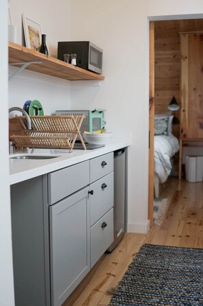Eine Küche mit weißer Arbeitsplatte, grauen Schränken, einem Holzbodenregal und einer Mikrowelle.