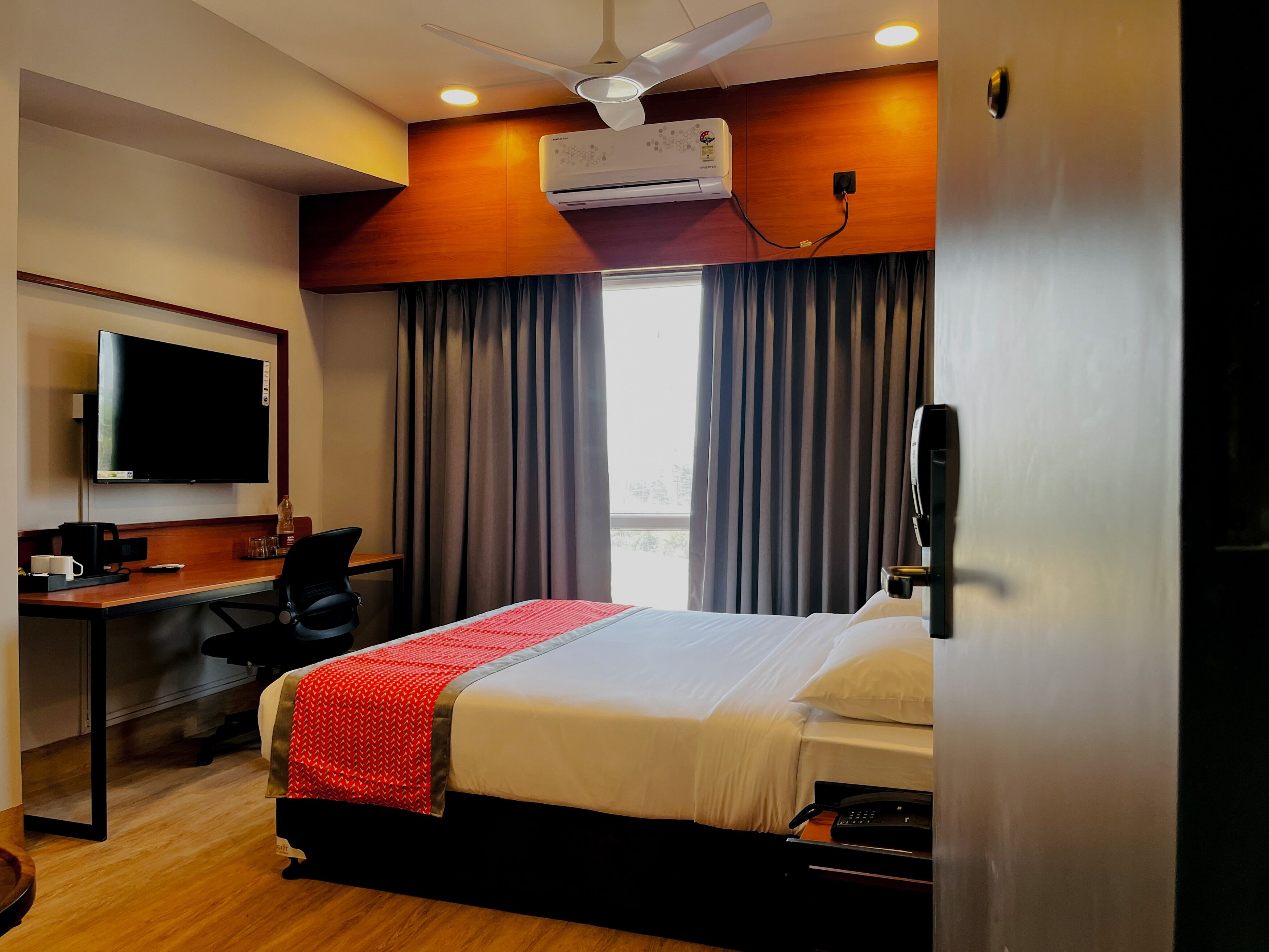 A hotel room with a bed, a desk, a chair, a television, and an air conditioning unit.