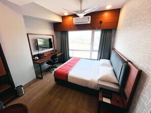 Une chambre d’hôtel équipée d’un lit, d’un bureau avec un ordinateur, d’une télévision et d’un ventilateur de plafond.