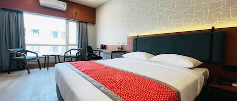 Quarto de hotel com cama, escrivaninha, duas cadeiras, mesa de cabeceira e janela com cortinas.