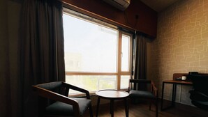 A room with a large window, two chairs, a small table, and a wooden floor. - The Citi Residenci Hotel Palasdiha (Durgapur)