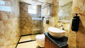 A bathroom with a marble wall, a white sink, a wooden cabinet, and a black bottle of lotion. - The Citi Residenci Hotel Palasdiha (Durgapur)