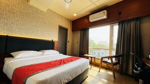 A hotel room with a bed, a desk, a chair, an air conditioning unit, and a window with curtains. - The Citi Residenci Hotel Palasdiha (Durgapur)
