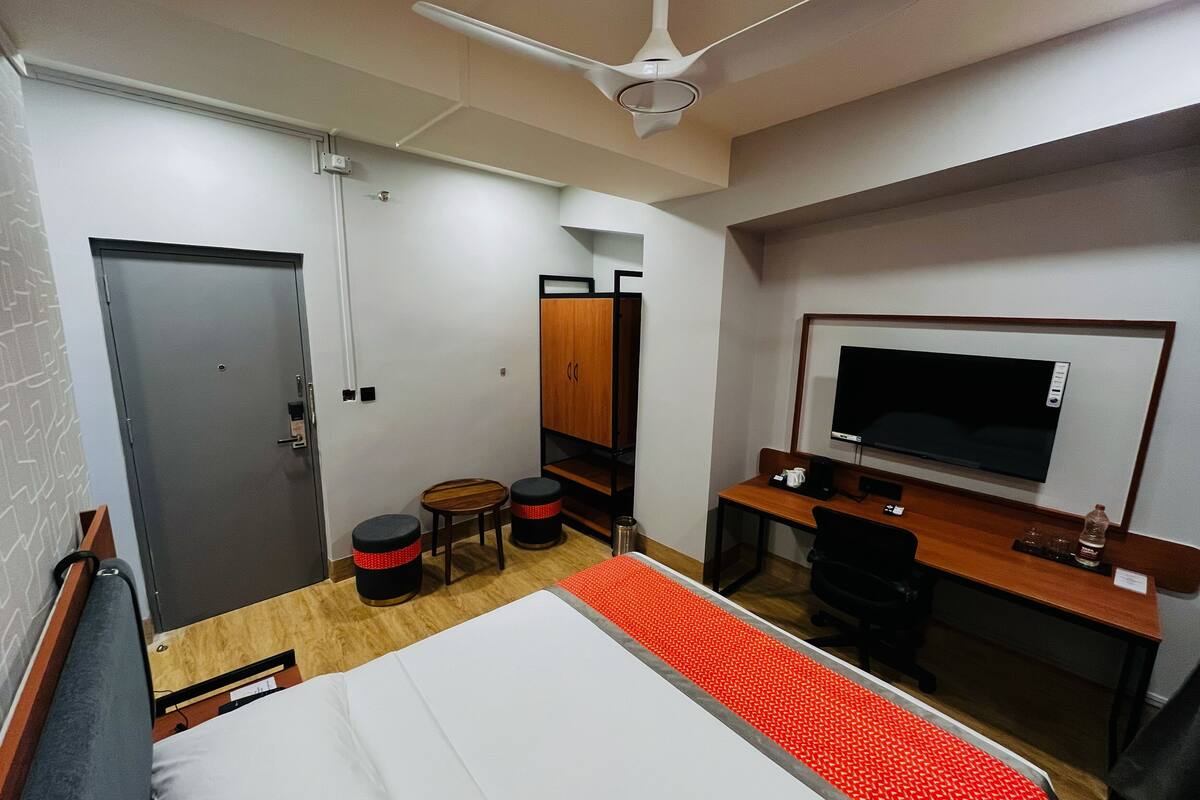 A hotel room with a bed, a desk with a TV, a wardrobe, and a ceiling fan.