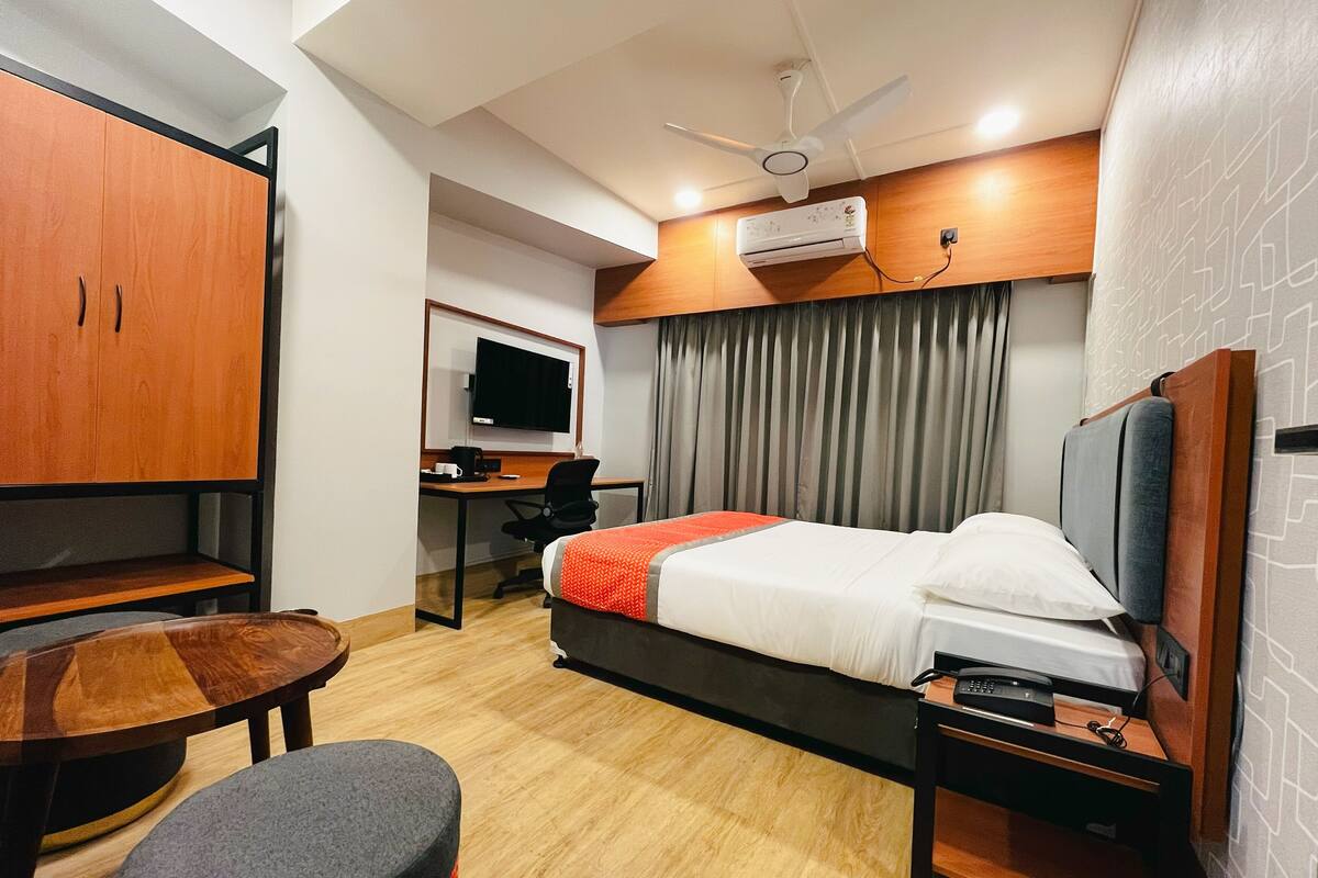 A hotel room with a bed, desk, chair, TV, and a ceiling fan.