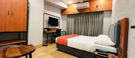 Habitación de hotel con cama, escritorio, silla, televisor y ventilador de techo.