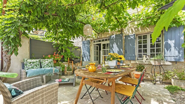 A patio area with wicker furniture, a wooden table, and a variety of potted plants. - Holiday Home “Chez Dominique” with Private Pool, Wi-Fi, and Air Conditioning (Saint-Rémy-de-Provence)