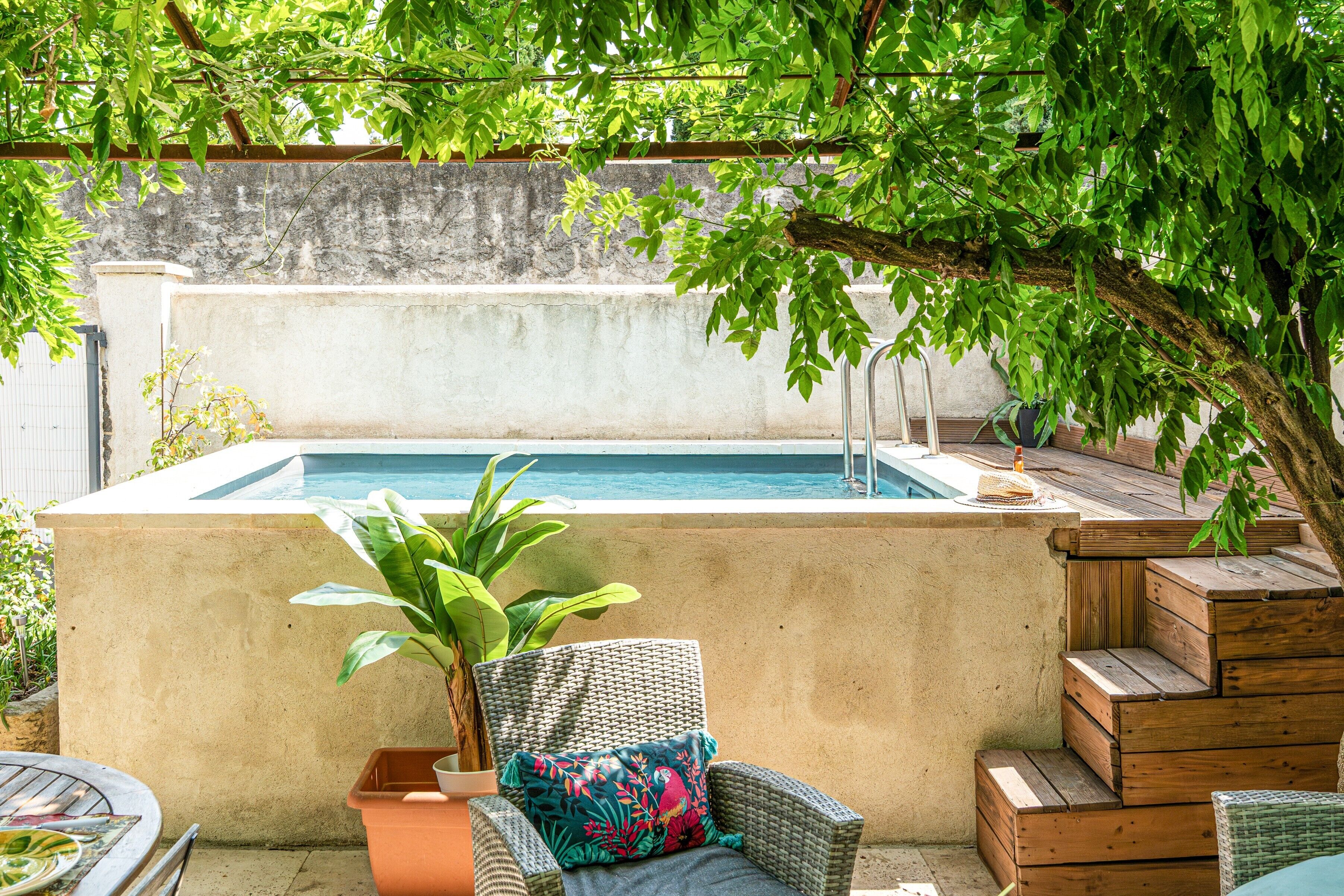Un espace piscine avec un mur en béton, une chaise en osier dotée d’un coussin et un escalier en bois.